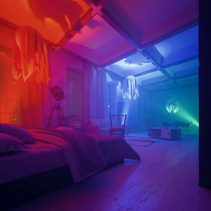 Futuristic bedroom with dramatic red, blue, and green lighting, minimal furniture, and surreal atmosphere.