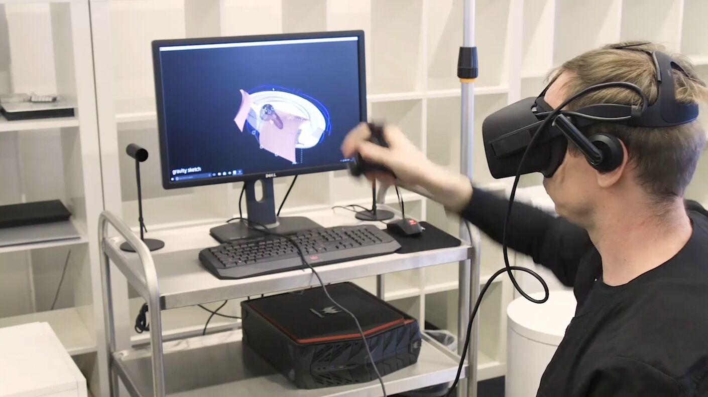 designer using a VR headset and controllers while modeling on a computer screen