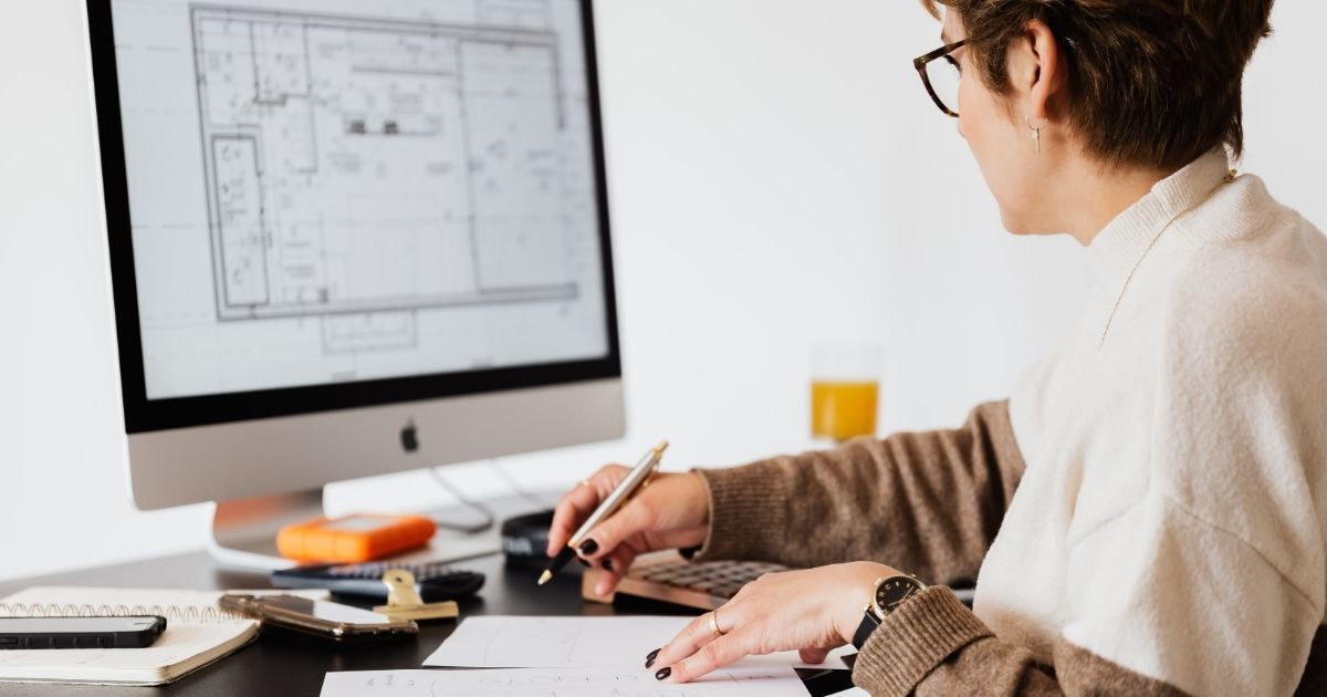 Designer reviewing building blueprints on a computer screen at a modern workspace.