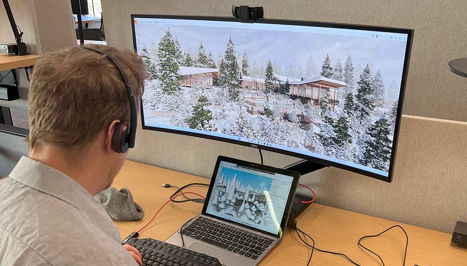 Man wearing a headset working at a desk with a curved monitor displaying a snowy 3D render and his laptop showing the Enscape model.