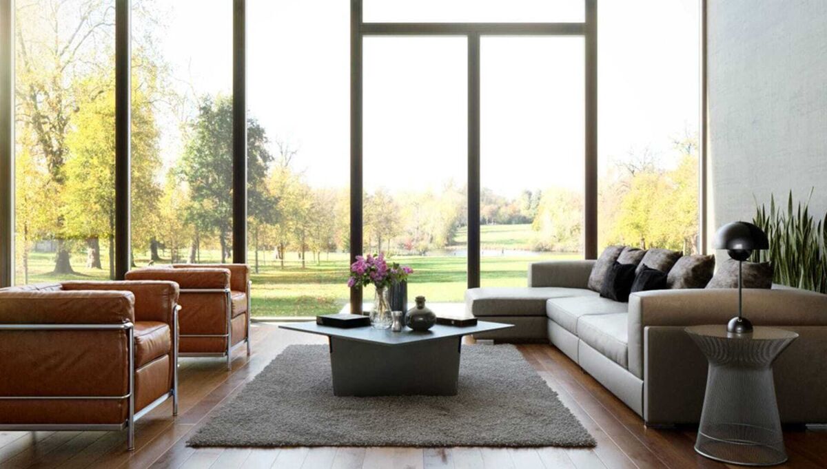 Spacious modern room with large windows, brown chairs, gray sofa, and garden scenery outside.